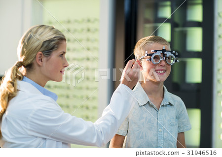 Female optometrist examining young patient with phoropter Female optometrist examining young patient with phoropter 31946516