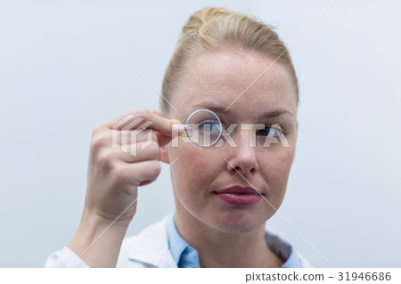 Female optometrist looking through magnifying glass Female optometrist looking through magnifying glass 31946686
