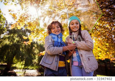 Low angle view of siblings holding umbrella in park Low angle view of siblings holding umbrella in park 31947402
