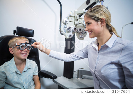 Female optometrist examining young patient with phoropter Female optometrist examining young patient with phoropter 31947694
