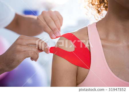 Physiotherapist sticking tape on female patient 31947852