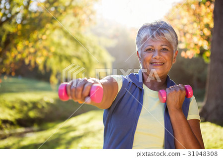 Smiling mature woman exercising with dumbbell Smiling mature woman exercising with dumbbell 31948308