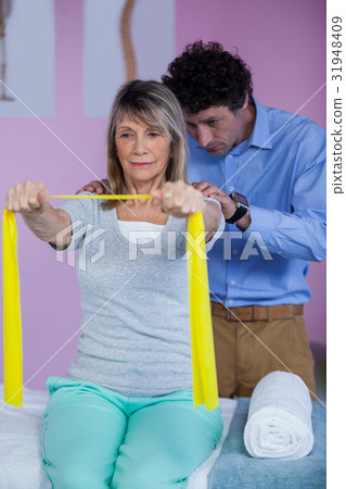 Senior woman training with exercise band assisted by physiotherapist Senior woman training with exercise band assisted by physiotherapist 31948409