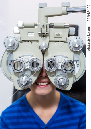 Young patient looking through phoropter during eye examination Young patient looking through phoropter during eye examination 31948432