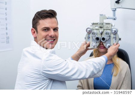 Smiling optometrist examining female patient on phoropter Smiling optometrist examining female patient on phoropter 31948597