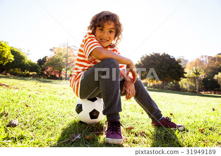 Portrait of smiling boy sitting on soccer ball 31949189