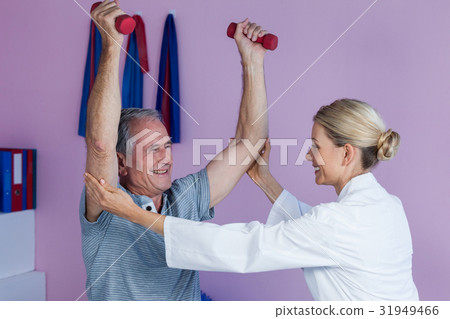 Physiotherapist assisting senior man to lift dumbbellÂ 31949466