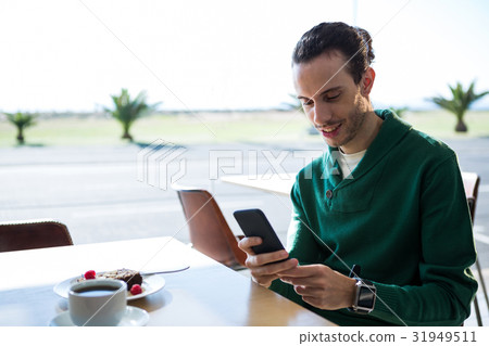 Man using mobile phone with cake and cup of coffee on table 31949511