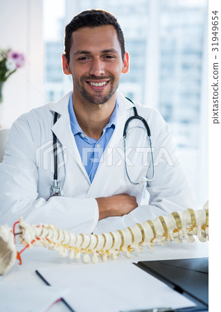 Portrait of smiling physiotherapist sitting with spine model Portrait of smiling physiotherapist sitting with spine model 31949654