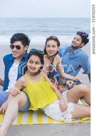 a group of four people is sitting on a carpet on seaside, looking at something 31950203