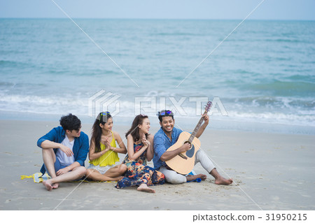 A man is playing the guitar and three his friends are listening on the beach 31950215