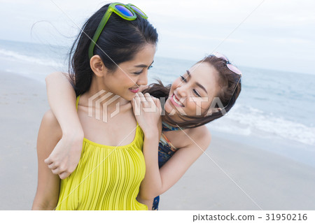 a girl is putting her arms on another girl's shoulder, smiling on the beach 31950216