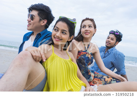 four people are sitting, looking at something together on the beach 31950218