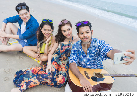 four people are sitting, smiling and taking selfie on the beach four people are sitting, smiling and taking selfie on the beach 31950219