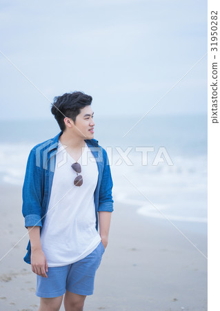 a photo of a young man standing and smiling in seaside a photo of a young man standing and smiling in seaside 31950282