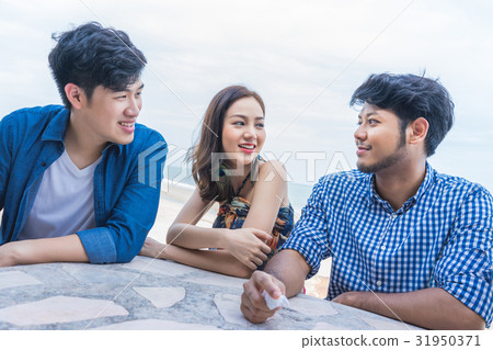 A girl and two men are sitting, talking together near the beach 31950371