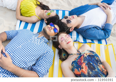A group of four people is relaxing and lying on the beach. 31950391