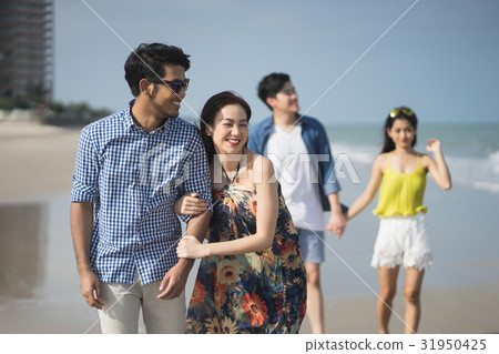 A couple is arm in arm and another one is holding hand on the beach. A couple is arm in arm and another one is holding hand on the beach. 31950425
