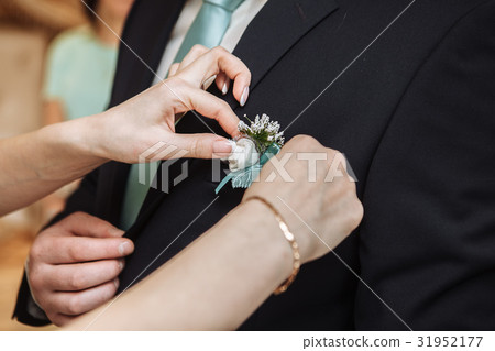 Woman pinning the boutonniere on the groom's 31952177