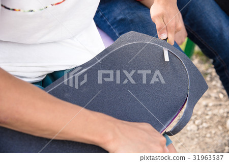 Boy cuts the griptape on a skateboard 31963587