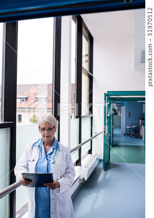 Doctor standing in corridor looking at clipboard Doctor standing in corridor looking at clipboard 31970512