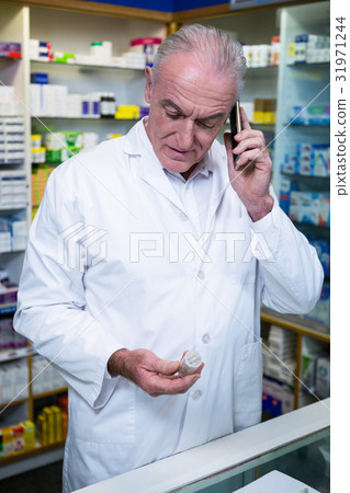 Pharmacist talking on mobile phone while checking medicine Pharmacist talking on mobile phone while checking medicine 31971244