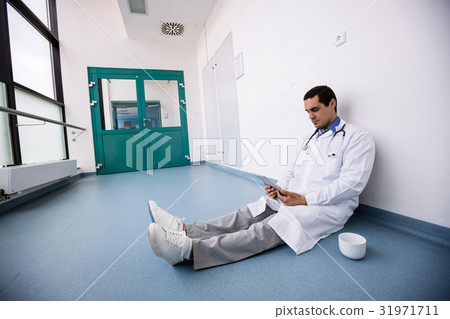 Doctor sitting on floor and using digital tablet in corridor Doctor sitting on floor and using digital tablet in corridor 31971711