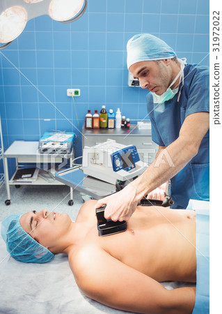Male surgeon resuscitating an unconscious patient with a defibrillator 31972022
