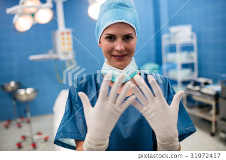 Portrait of female surgeon showing surgical gloves in operation room 31972417