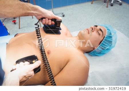 Male surgeon resuscitating an unconscious patient with a defibrillator 31972419