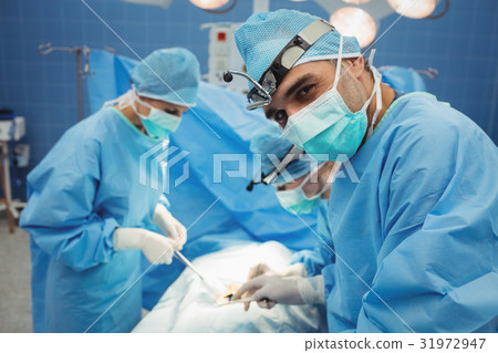 Surgeon looking at camera while colleagues performing operation 31972947
