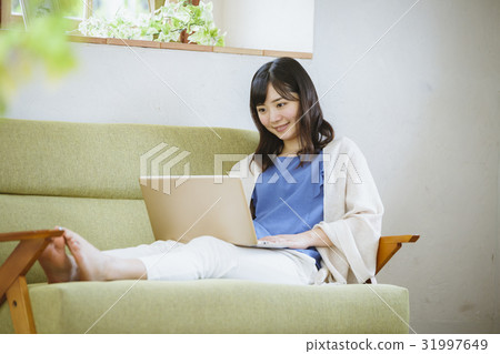 使用便攜式計算機的婦女在沙發 使用便攜式計算機的婦女在沙發 31997649