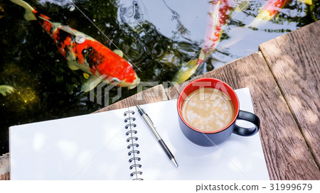 hot coffee, book, and pen place near a fancy carp pond. hot coffee, book, and pen place near a fancy carp pond. 31999679