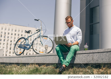 Handsome employee sitting on stairs and typing on Handsome employee sitting on stairs and typing on 32002182