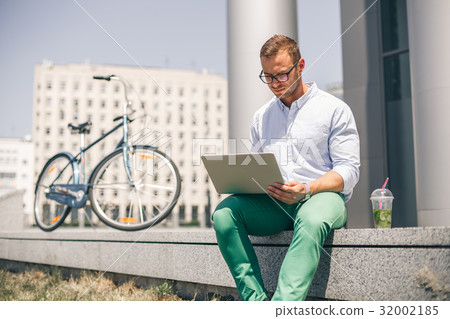 Handsome employee sitting on stairs and typing on 32002185