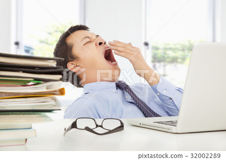 Exhausted young businessman yawning at work Exhausted young businessman yawning at work 32002289