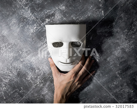 Hand holding white mask on gray grunge background. 32017583