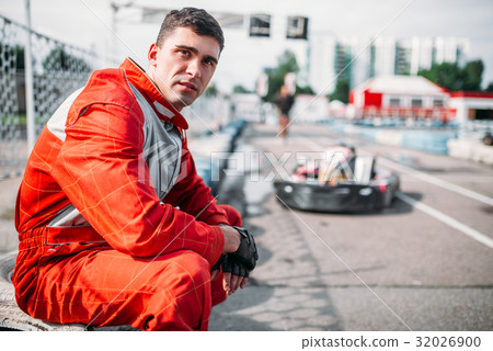 Karting racer sits on a tire, kart on background 32026900