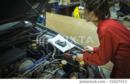 Female mechanic testing car battery with 32027413