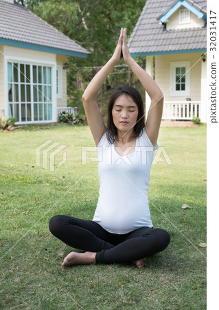 asian pregnant woman practicing yoga on green grass in front of her house. meditating on maternity. concept of healthy lifestyle and relaxation. 32031417