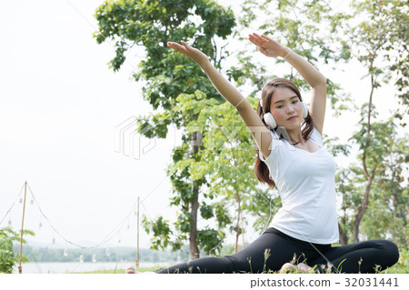 asian pregnant woman practicing yoga while listening to music on green grass in public park. concept of prenatal exercise, maternity, fitness, healthy lifestyle and relaxation. 32031441