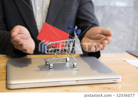 male showing a credit card in mini supermarket cart trolley full of coins on laptop computer for online shopping. businessman purchase goods from internet. man make payment on bank website male showing a credit card in mini supermarket cart trolley full of coins on laptop computer for online shopping. businessman purchase goods from internet. man make payment on bank website 32036877
