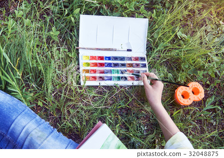 Young girl painting sitting on grass in summer 32048875