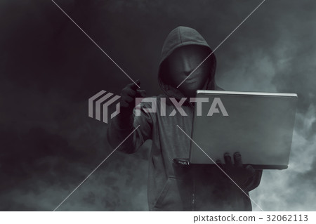 Portrait of hooded hacker with mask holding laptop 32062113
