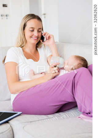 Mother talking on mobile phone while feeding her baby with milk bottle 32062620