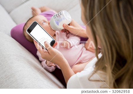 Mother using mobile phone while feeding her baby with milk bottle Mother using mobile phone while feeding her baby with milk bottle 32062958