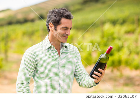 Smiling vintner looking at bottle of wine Smiling vintner looking at bottle of wine 32063107