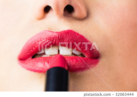 Beautiful woman applying red lipstick on lips against black background 32063444