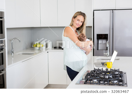 Mother carrying her baby in kitchen at home Mother carrying her baby in kitchen at home 32063467