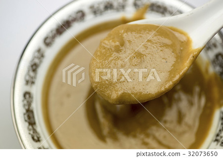 Pick up a tablespoon of white sesame sauce from a porcelain bowl 32073650